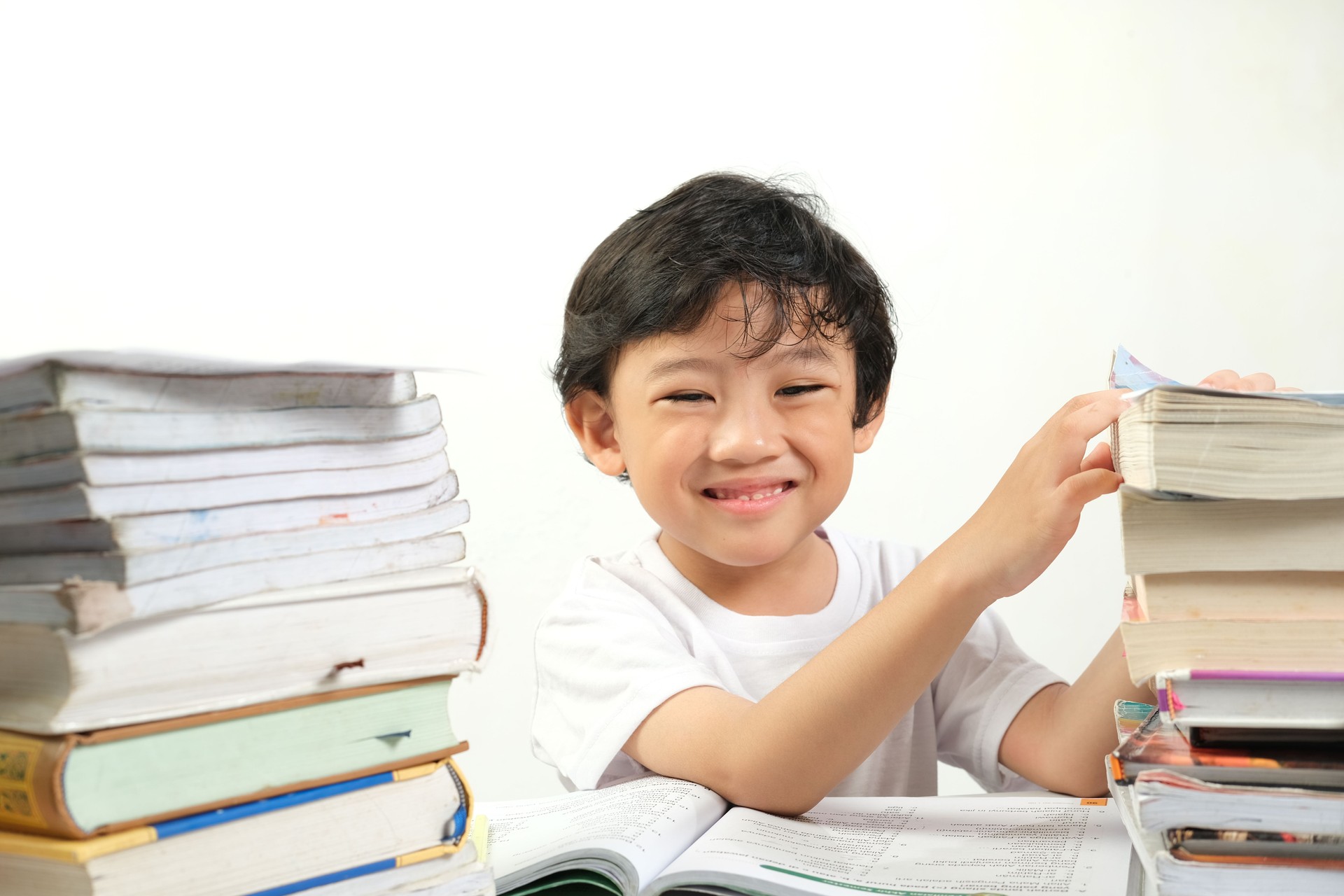 A cheerful young boy studying surrounded by stacks of books, smiling brightly.
